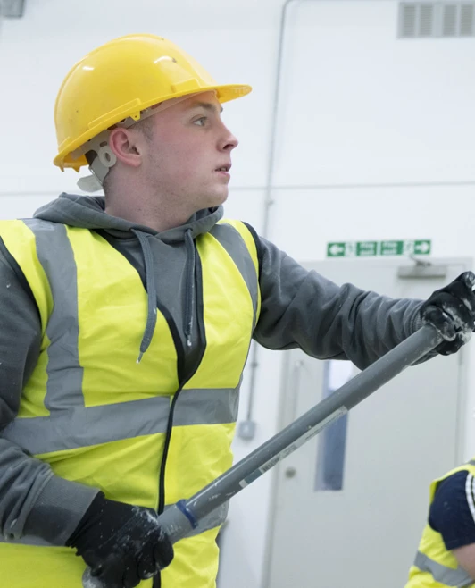 Student using a paint roller to coat a tall wall in a white room Student using a paint roller to coat a tall wall in a white room